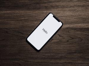 Black Iphone 7 on Brown Table with word "Hello" on it.