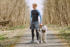 Man stands in park ready to jog with his dog.