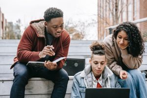 Multiracial students studying on netbook with notebook on steps.